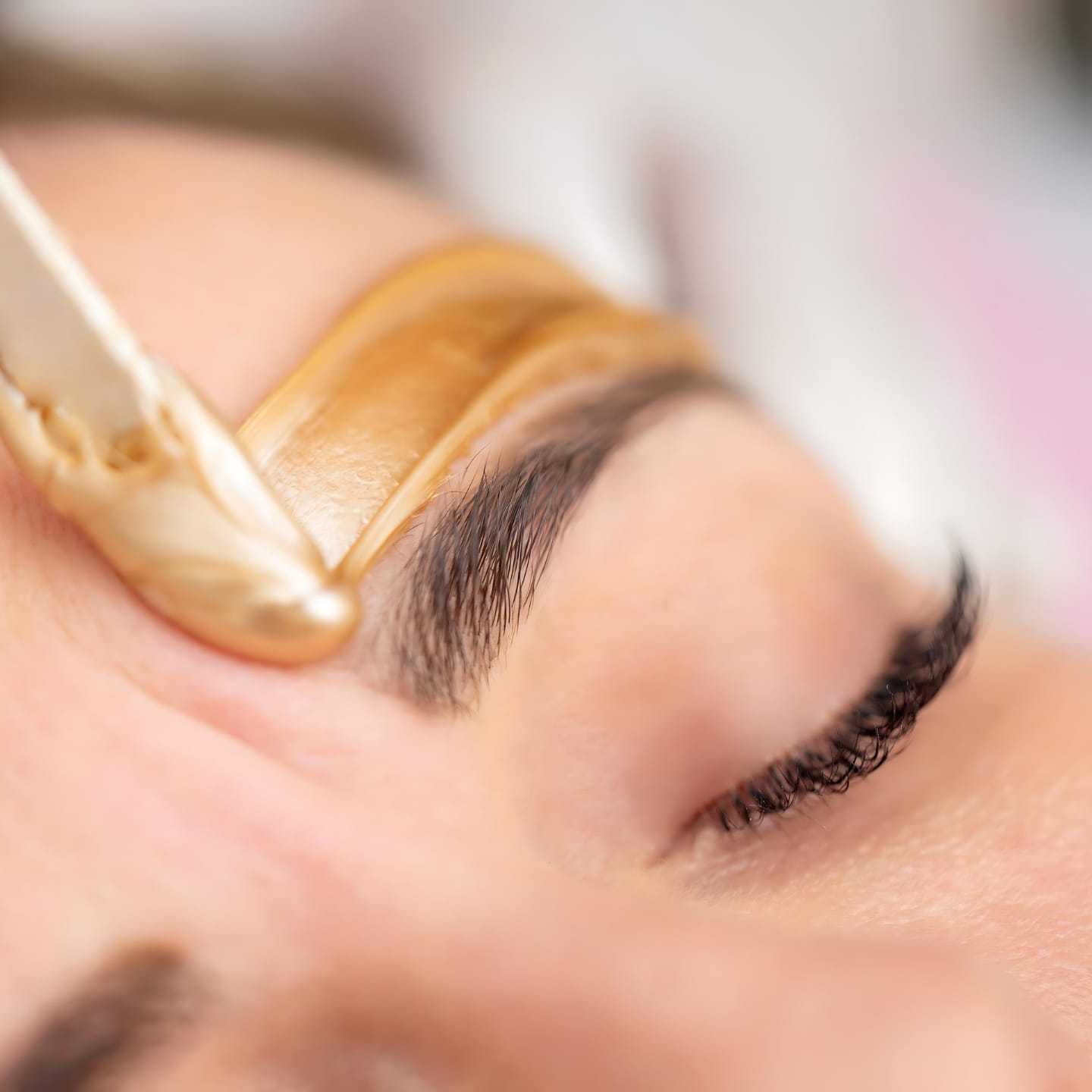 Close-up of a person's brow being shaped with wax during a beauty treatment.